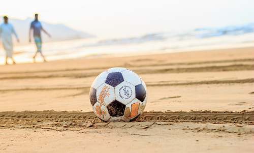 soccer ball soccer ball on brown sand with two man in the background sand